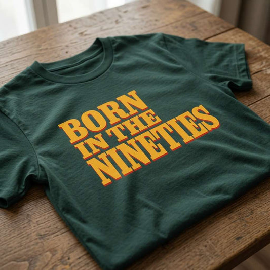 Green Born in the Nineties t-shirt laid flat on a wooden surface showing the full bold yellow lettering, mens fun 90s movie inspired born in tee that every cheeky lad will claim