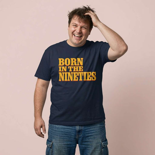 Man laughing with one hand in his hair while wearing a navy Born in the Nineties t-shirt in bold yellow lettering, mens fun 90s movie inspired age design
