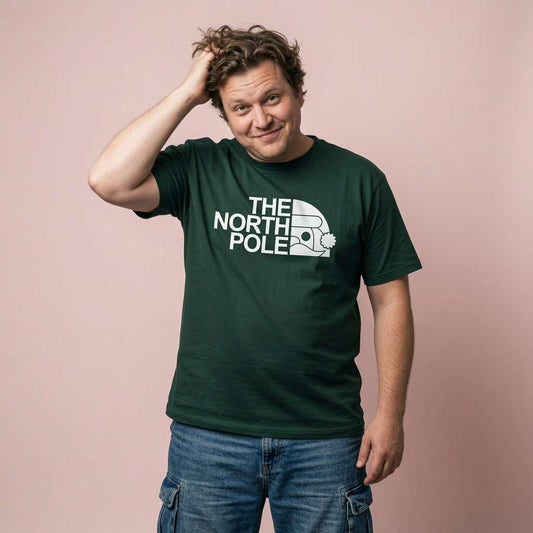 Man with one hand in his hair while wearing a glazed green The North Pole t-shirt with a North Face-style Santa hat logo, fun and witty Christmas design