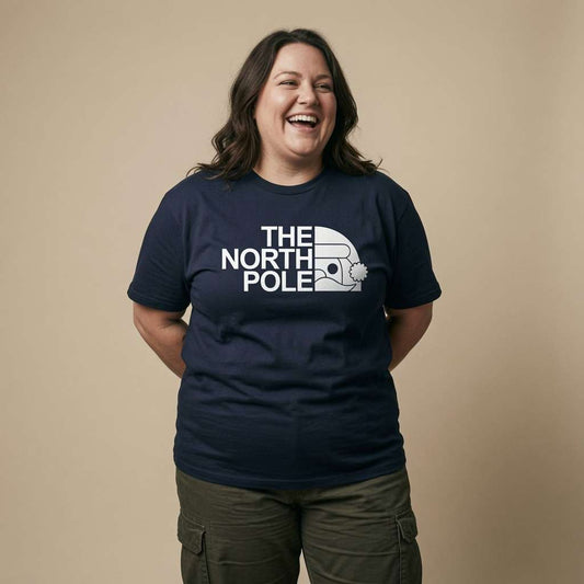 Woman laughing with hands behind her back while wearing a navy The North Pole t-shirt with a North Face-style Santa hat logo, funny and cheeky Santa xmas day pub shirt