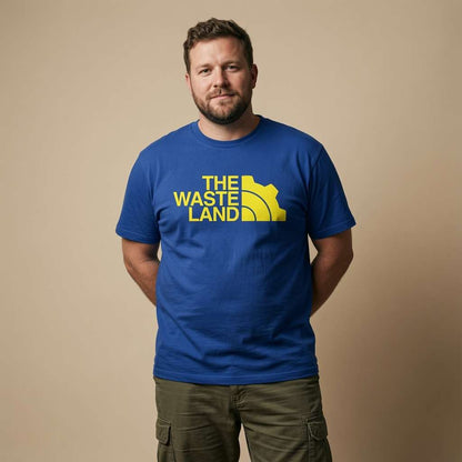 Man standing with hands behind his back while wearing a blue The Wasteland t-shirt with a North Face-style gear logo, mens gamer vault design
