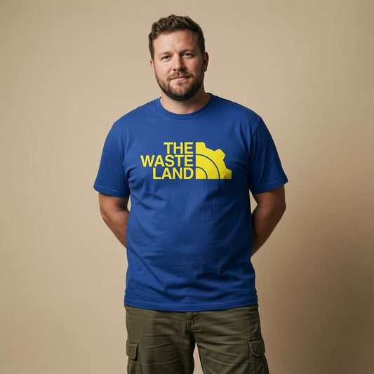 Man standing with hands behind his back while wearing a blue The Wasteland t-shirt with a North Face-style gear logo, mens gamer vault design