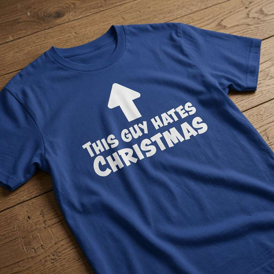 Blue This Guy Hates Christmas t-shirt laid flat on a wooden surface showing the full anti-Christmas slogan, mens pub banter text shirt