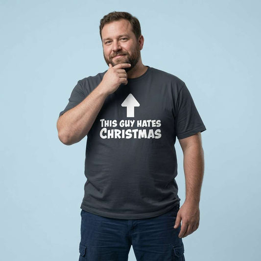 Man with one hand on his chin while wearing an ink grey This Guy Hates Christmas t-shirt, mens cheeky Christmas day banter slogan tee that every no-nonsense lad will claim