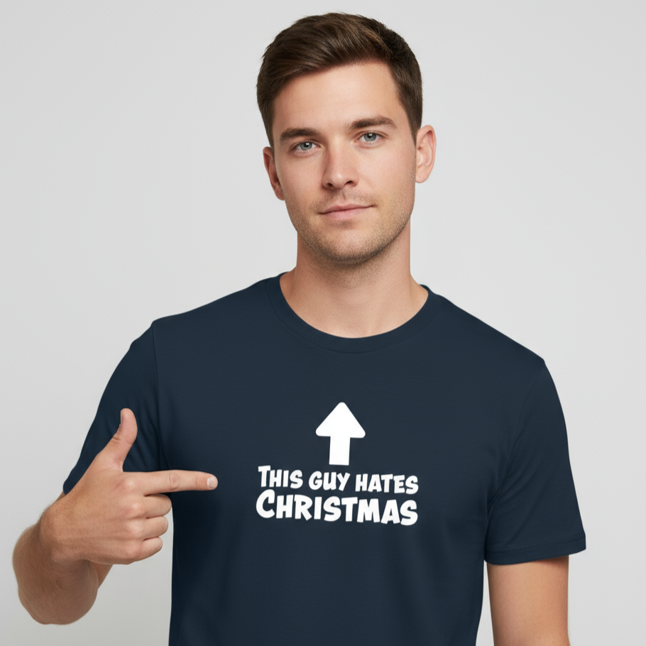 A man in a navy blue T-shirt with bold white text and an arrow pointing up reads, "This guy hates Christmas." He points to the text with a neutral expression.