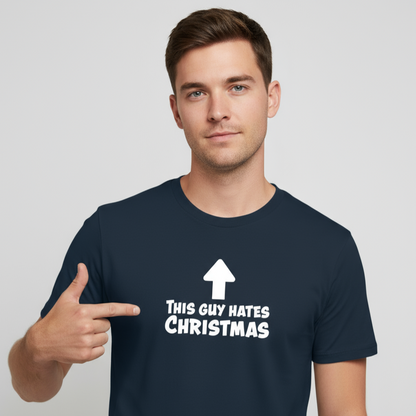 A man in a navy blue T-shirt with bold white text and an arrow pointing up reads, "This guy hates Christmas." He points to the text with a neutral expression.