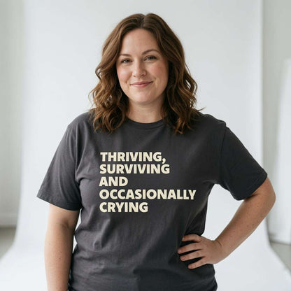 Woman standing with one hand on her hip in a black Thriving, Surviving and Occasionally Crying t-shirt, funny and witty ladies slogan design full of pure attitude