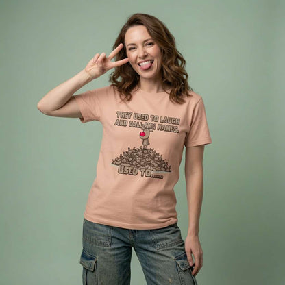Woman sticking her tongue out and making a peace sign in a peach They Used to Laugh and Call Him Names t-shirt, witty ladies psycho reindeer design full of pure attitude