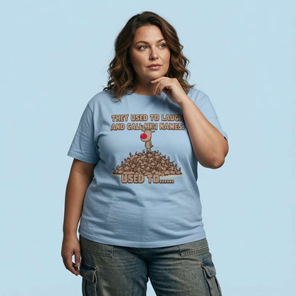 Woman looking to the side with one hand on her chin while wearing a sky blue They Used to Laugh and Call Him Names t-shirt featuring Rudolph on a pile of antlers, ladies dark Christmas Day humour design