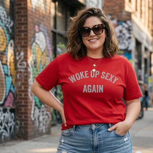Woman smiling with one hand in her pocket and sunglasses on while wearing a red Woke Up Sexy Again t-shirt outdoors, funny witty ladies quote design