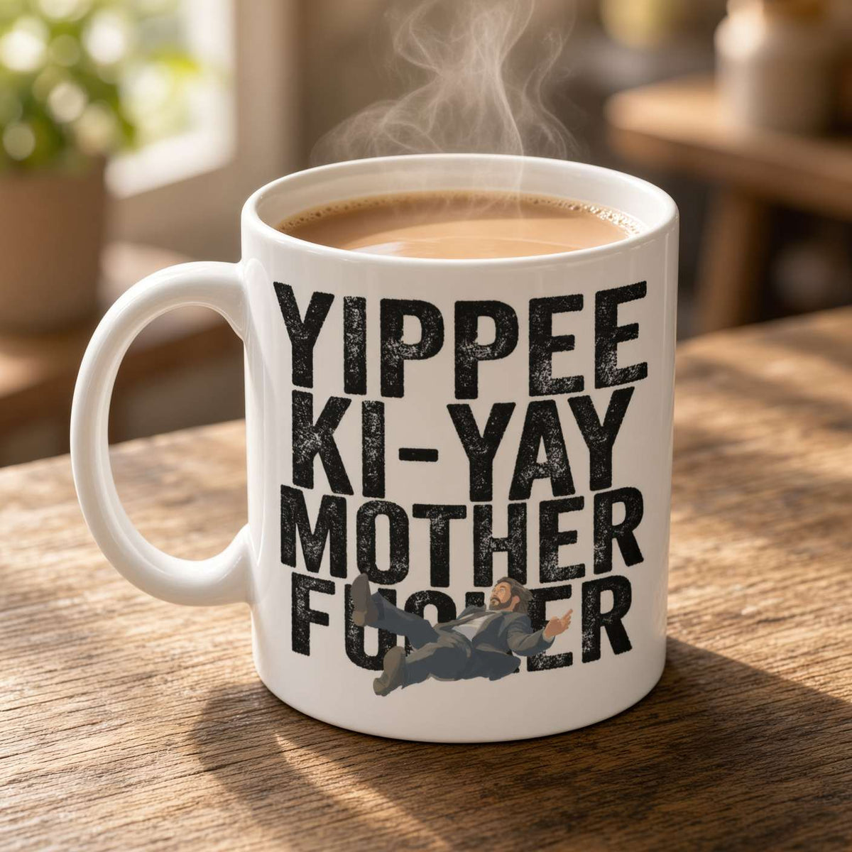 A steaming white coffee mug on a sunlit wooden table reads “Yippee Ki-Yay Mother F***er,” with a small action scene graphic, giving a bold, playful tone.