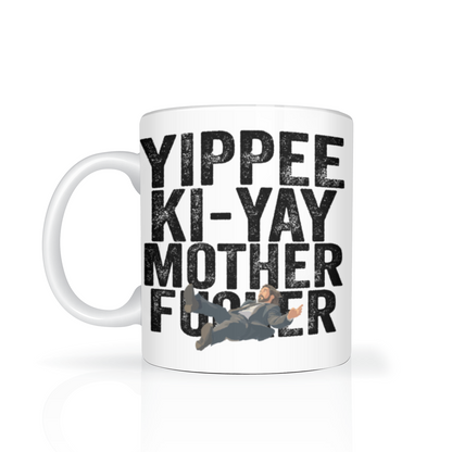 White coffee mug with bold black “Yippee-ki-yay, mother…” text and a small action hero illustration, evoking humorous, irreverent movie-themed bravado.