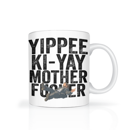 White ceramic mug with bold black “Yippee Ki-Yay Mother F—er” text and a small action-movie figure graphic, giving it a cheeky, irreverent tone.