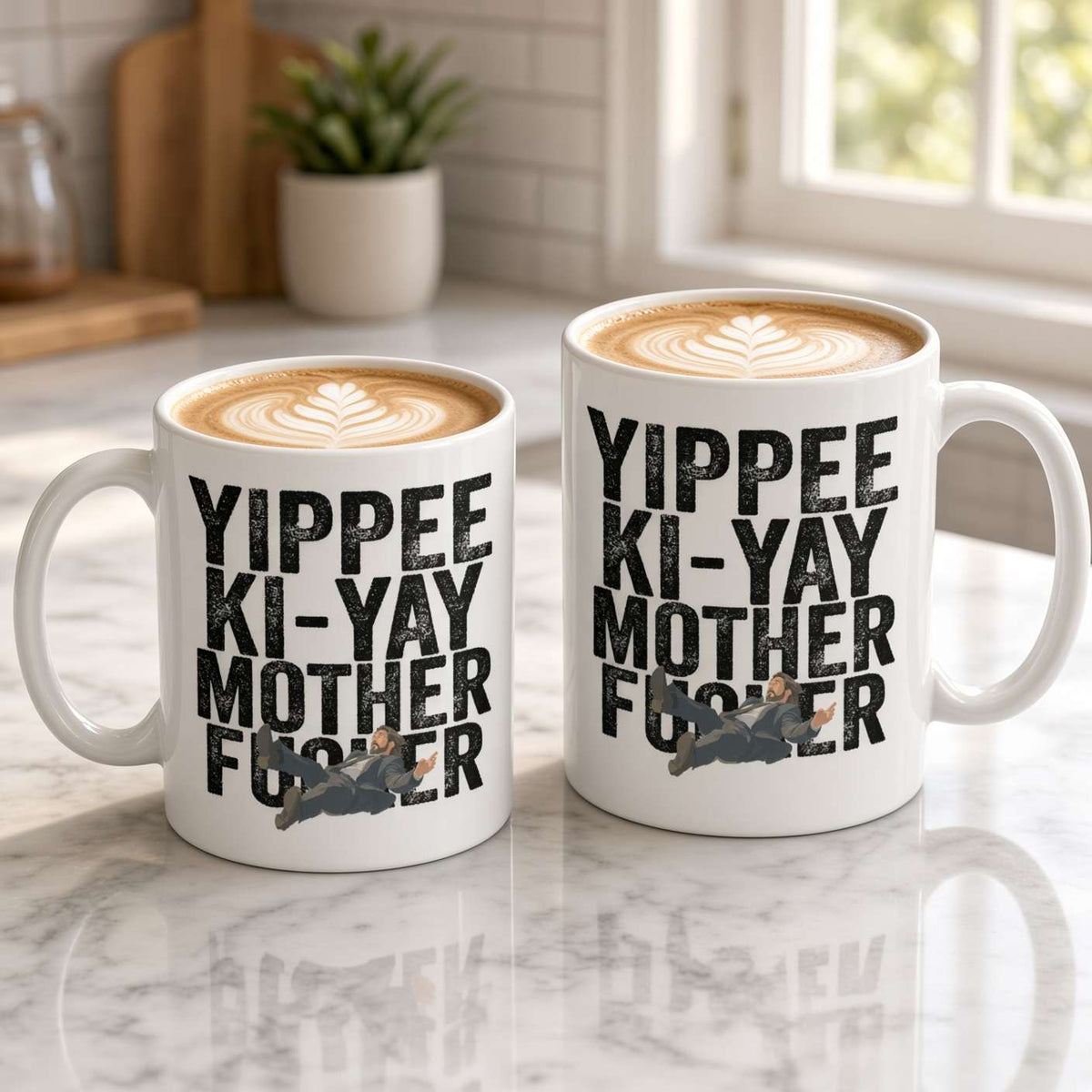 Two white latte mugs with leaf-art foam and bold “Yippee Ki-Yay Mother F…” lettering sit on a marble counter, creating a playful kitchen scene.