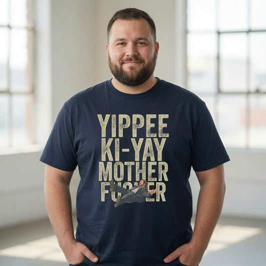 Man standing with both hands in his pockets while wearing a ink grey Yippee Ki-Yay Mother Fucker t-shirt featuring John McClane falling, fun mens Nakatomi Xmas design