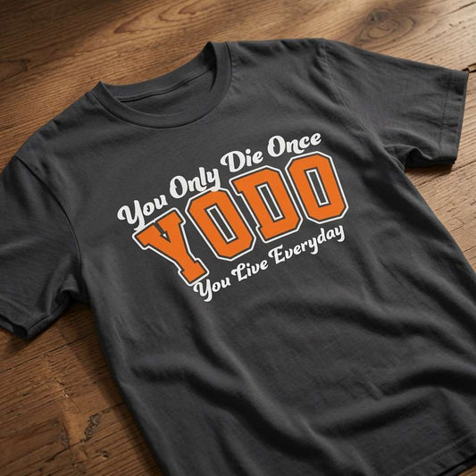 Black YODO t-shirt laid flat on a wooden surface showing the full You Only Die Once / You Live Everyday slogan, funny mens positive motivational slogan shirt full of pure attitude