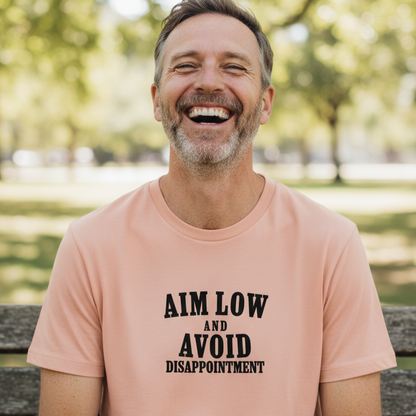 Man wearing a peach t-shirt that reads 'aim low and avoid disappointment' whilst in a park