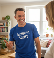 Man wearing a blue t-shirt with 'ALWAYS RIGHT' text, smiling and talking to a woman in a living room.
