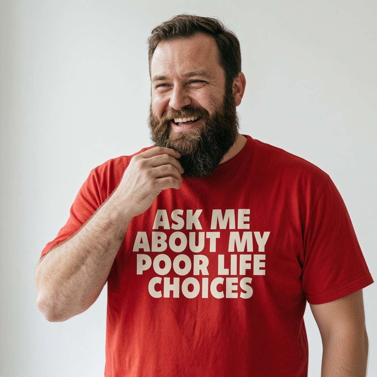 A smiling bearded man wearing a red t-shirt with the text 'ASK ME ABOUT MY POOR LIFE CHOICES' in white, posing against a light gray background.