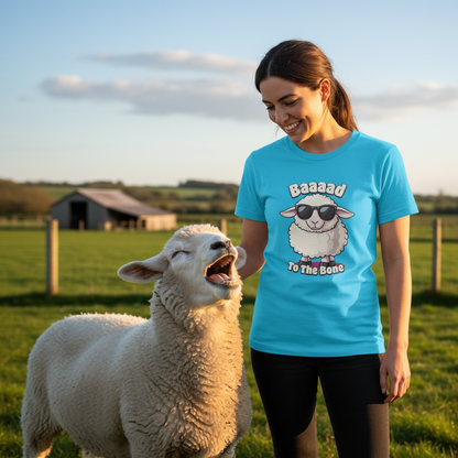 Woman wearing a blue t-shirt with a sheep graphic and text, standing next to a sheep in a field.