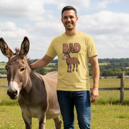 Man wearing a yellow t-shirt with a donkey graphic and 'BAD' text, standing next to a donkey in a field.
