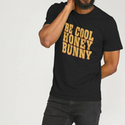 Person wearing a black t-shirt with 'BE COOL HONEY BUNNY' slogan in yellow on a plain background, in a pulp fiction style font.