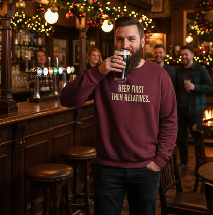 Man in a pub wearing a sweatshirt with 'Beer First Then Relatives' text, holding a pint.