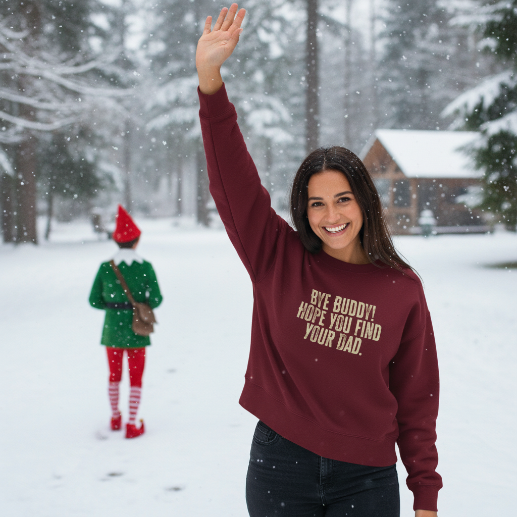 Woman in a snowy landscape wearing a maroon sweatshirt with the text 'by buddy hope you find your dad', waving at someone in an elf costume.