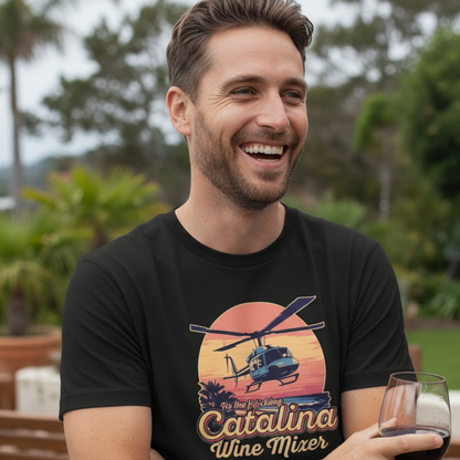Man wearing a black Catalina Wine Mixer t-shirt featuring a retro sunset and helicopter graphic design while holding a glass of red wine.