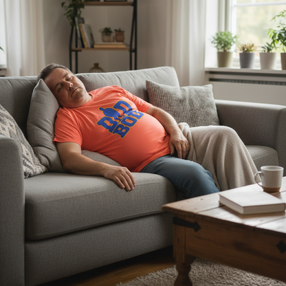 Man resting on a couch wearing an orange shirt with blue text in a cozy living room.