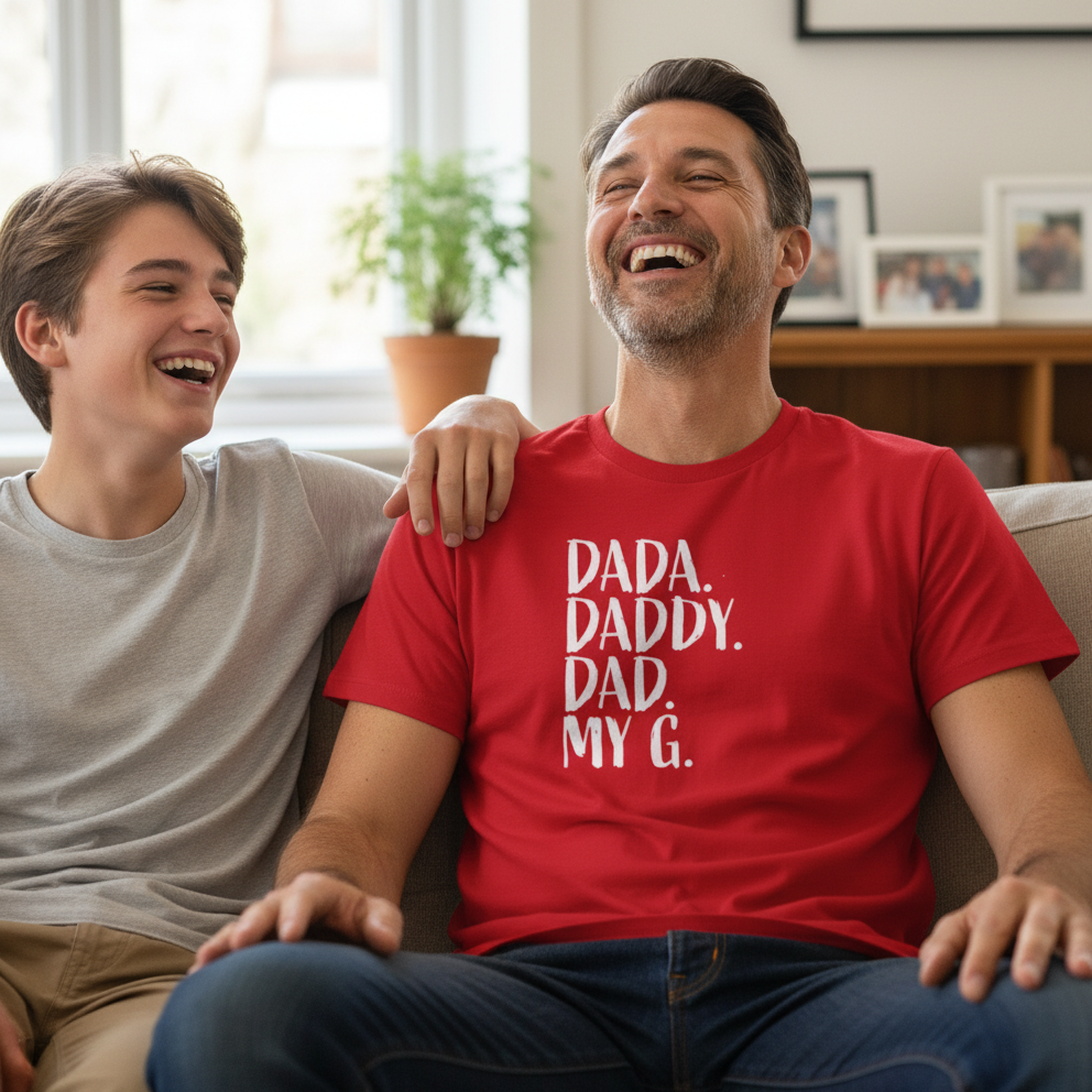 Man wearing a red t-shirt with 'Dada. Daddy. Dad. My G.' text, sitting on a couch with a young boy.