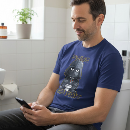 Man sitting on a toilet using a phone, wearing a blue t-shirt with a graphic design.