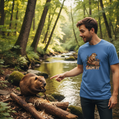 Man in a blue t-shirt with a beaver graphic and 'DAM IT' text standing next to a beaver by a stream in a forest.