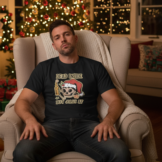 Man sitting in a chair wearing a black t-shirt with a Christmas-themed design in a cozy living room with a Christmas tree.