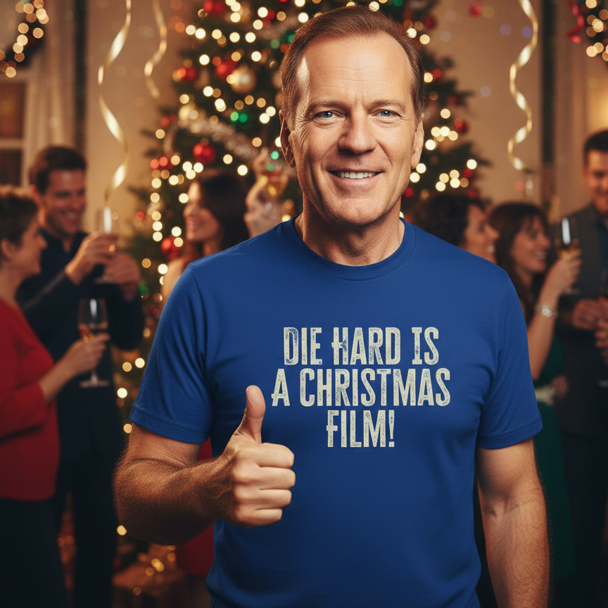 Man wearing a blue t-shirt with 'Die Hard is a Christmas film!' text, giving a thumbs up in a festive setting.