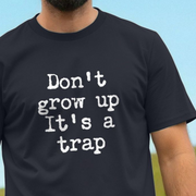 Black slogan t-shirt with white text 'Don't grow up It's a trap' against a light blue sky.