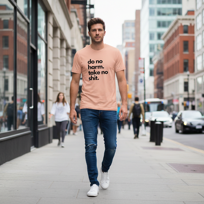 Man walking on a city street wearing a peach t-shirt with the slogan 'do no harm take no shit'