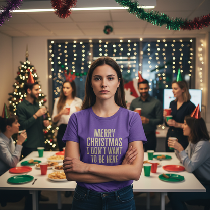 A woman in a purple shirt with "Merry Christmas, I Don’t Want to Be Here" stands with arms crossed at a festive office party. Her expression is serious, contrasting with colleagues in party hats enjoying the celebration. Decor includes a lit Christmas tree and string lights, creating a cheerful yet ironic atmosphere.