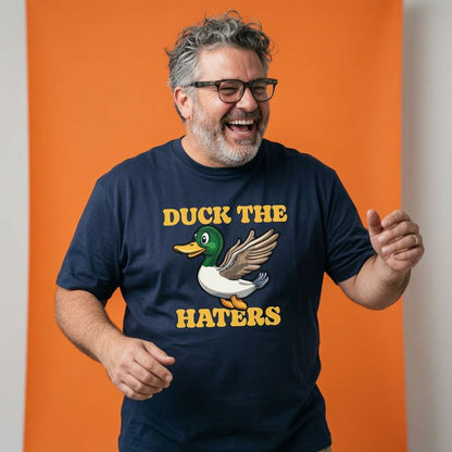 Man laughing with both hands raised while wearing a navy Duck The Haters t-shirt featuring a cartoon mallard duck, funny mens duck pun graphic shirt full of pure attitude