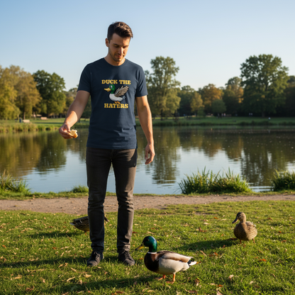 Man in a park with ducks near a pond wearing a t-shirt with text.
