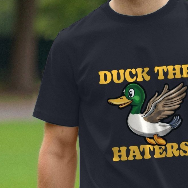 Black t-shirt with a duck graphic and text 'DUCK THE HATERS' on a blurred green background