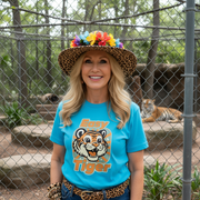 Woman wearing a blue t-shirt with a tiger graphic, standing in front of a chain-link fence with a tiger in the background.