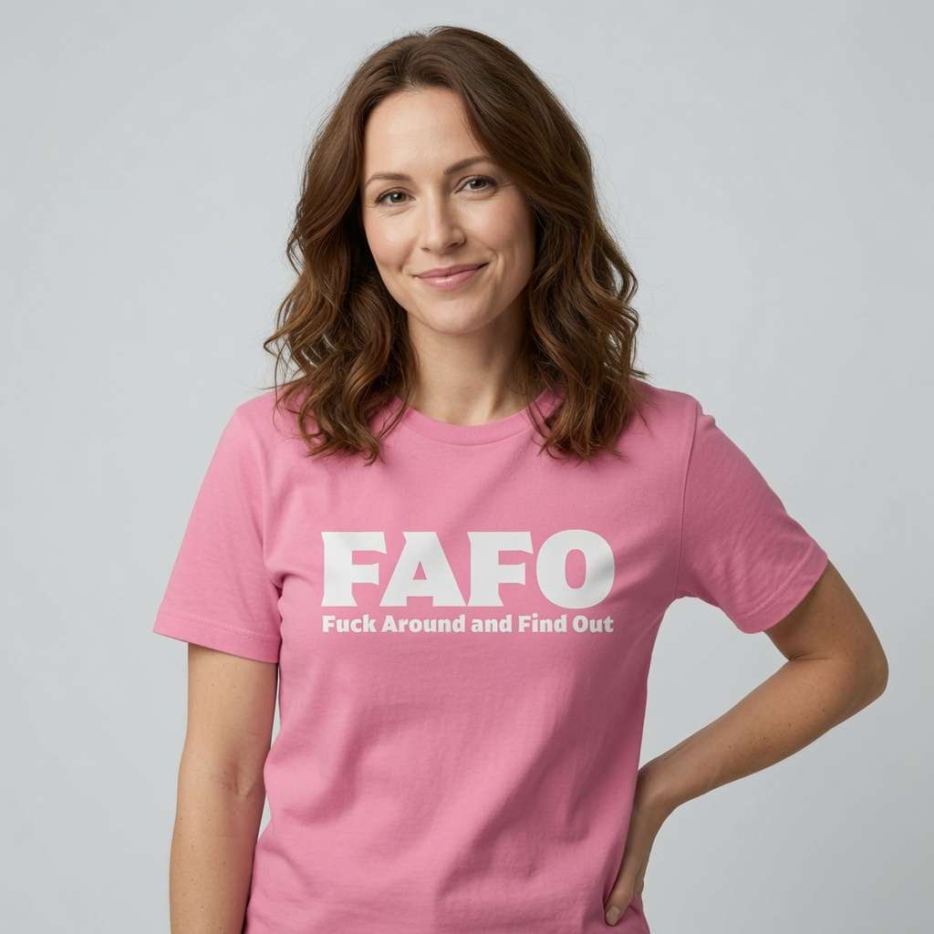 A woman with wavy brown hair wearing a pink crewneck t-shirt with the white printed text 'FAFO Fuck Around and Find Out' on the chest, posed against a light gray studio background.