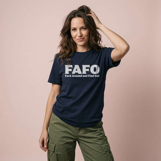 A woman modeling a navy blue t-shirt with the bold white text 'FAFO' and the phrase 'Fuck Around and Find Out' printed on the front, paired with olive green cargo pants against a solid pale pink background.