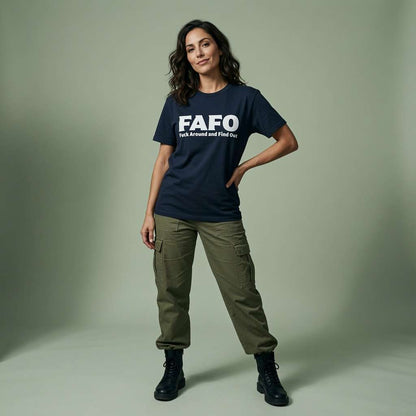 A woman modeling a navy blue graphic t-shirt with white text that reads 'FAFO talk around and find out', paired with olive green cargo pants and black boots, against a solid sage green studio background.