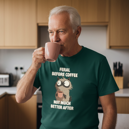 Man drinking from a pink mug in a kitchen wearing a green t-shirt with a humorous cat graphic and text.