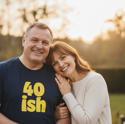 Man wearing a shirt with '40ish' and a woman embracing him outdoors.