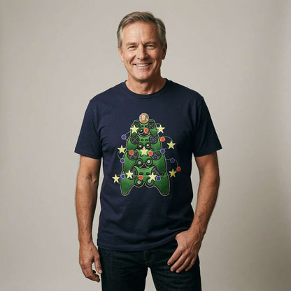 A smiling man wearing a navy blue t-shirt with a green Christmas tree game controller graphic, paired with dark jeans, standing against a neutral light gray background.