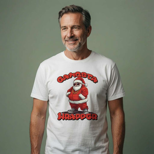 A smiling middle-aged man wearing a white graphic t-shirt with a cartoon Santa Claus and the text 'GANGSTA WRAPPER' in red, standing against a solid muted green-gray background.