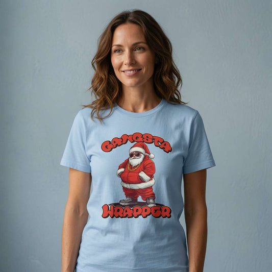 A woman wearing a light blue crewneck t-shirt with a graphic of a Santa Claus character and the text 'GANGSTA WRAPPA' in red, standing against a textured gray wall.